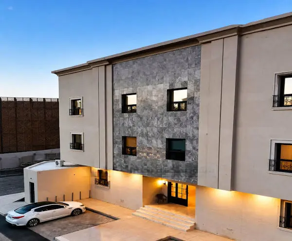 Three-storey stone-clad residential building with lit entrance steps and a car in the forecourt