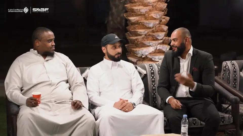 Three guests talking on a majlis sofa at an evening dinner, the Safwah Investment and SMBF logos in the corner of the frame